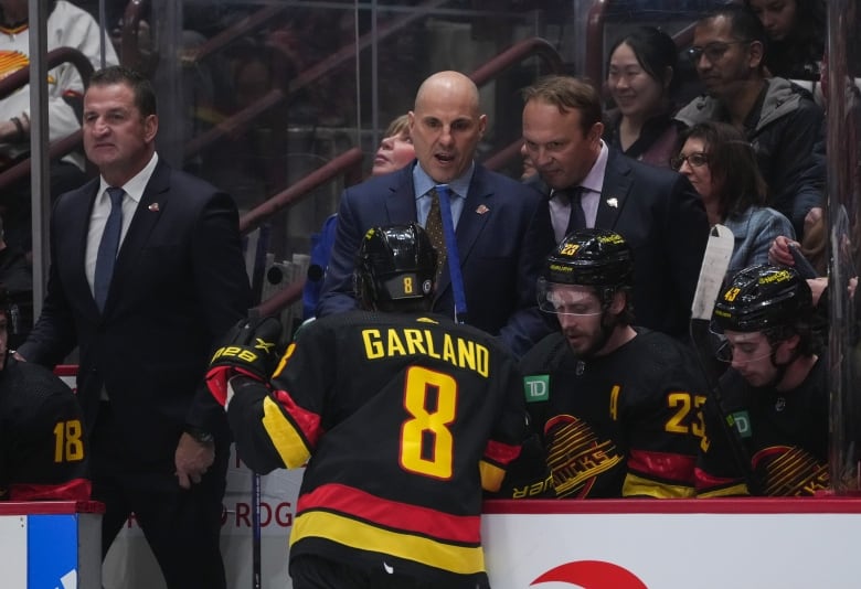 Vancouver Canucks head coach Rick Tocchet, back centre, talks to Conor Garland, centre, as defensive development coach Sergei Gonchar, right, listens while assistant coach Adam Foote, back left, stands behind the bench.