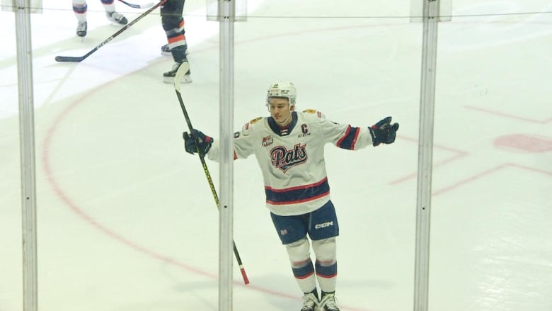 A hockey player is skating on the ice toward the boards, with his arms spread out and stick in hand, as he celebrates scoring a goal.