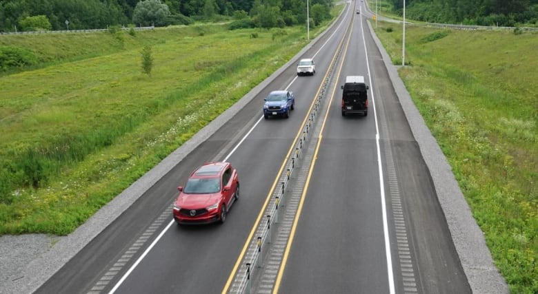 Several vehicles are seen from above making their way along a highway on a summer day.