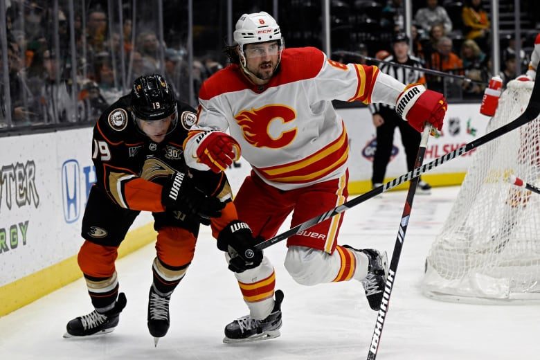 Two male ice hockey players battle for position with their shoulders together.