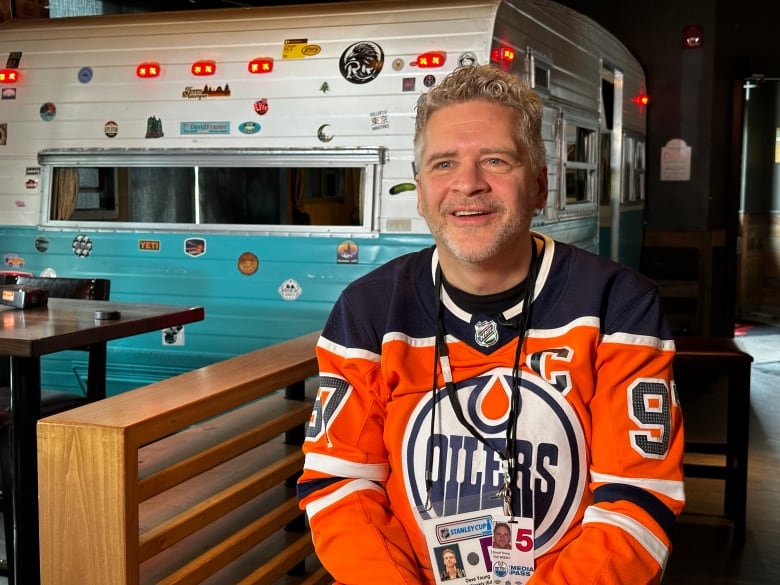 A man wearing an Edmonton Oilers jersey sits in front of a camper inside a restaurant.