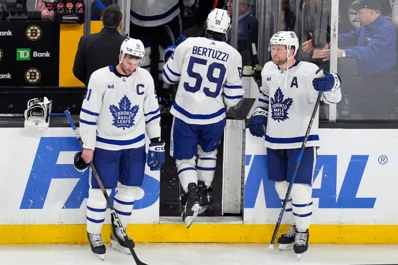 Three hockey players look dejected near the exit of a rink.