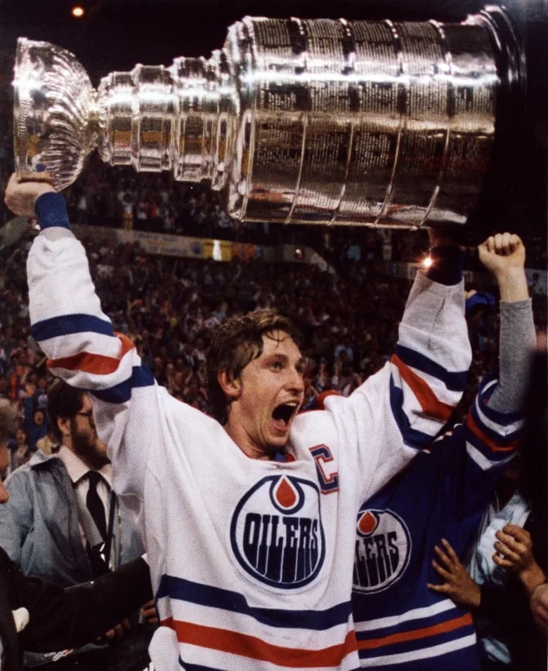 Man wearing Oilers jersey holding the Stanley Cup above his head.