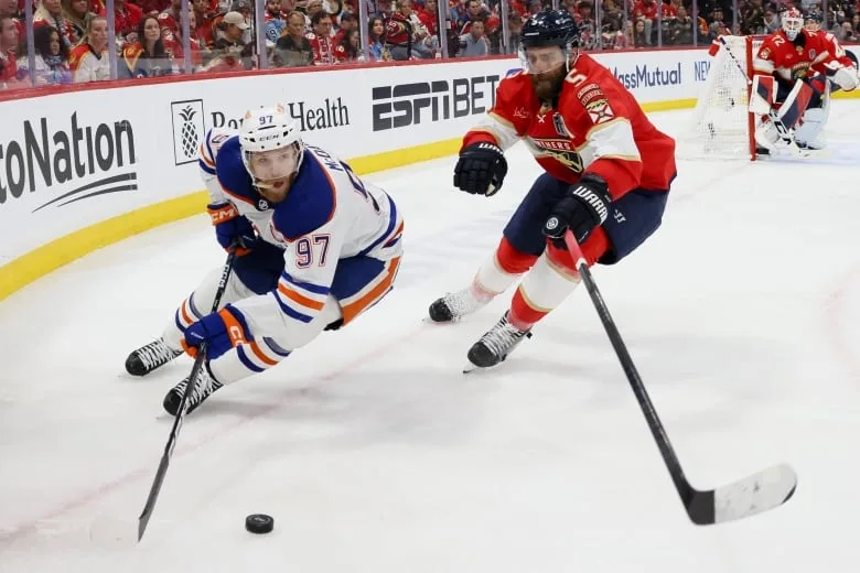 A hockey player skates with the puck as an opposing player defends.