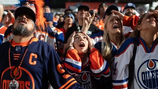 Sports fans react while looking up to watch a big screen.