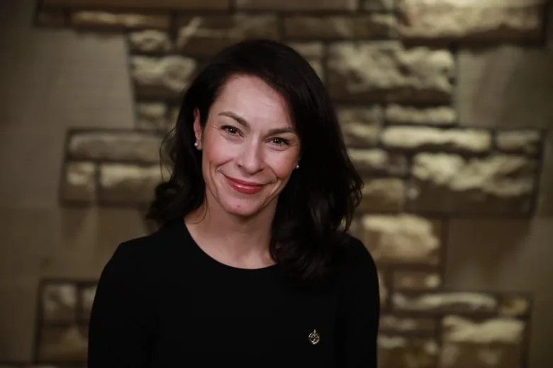 A woman in a dark dress smiles into a camera.