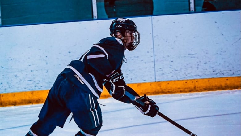 A hockey player skates in an arena, wearing a blue jersey.